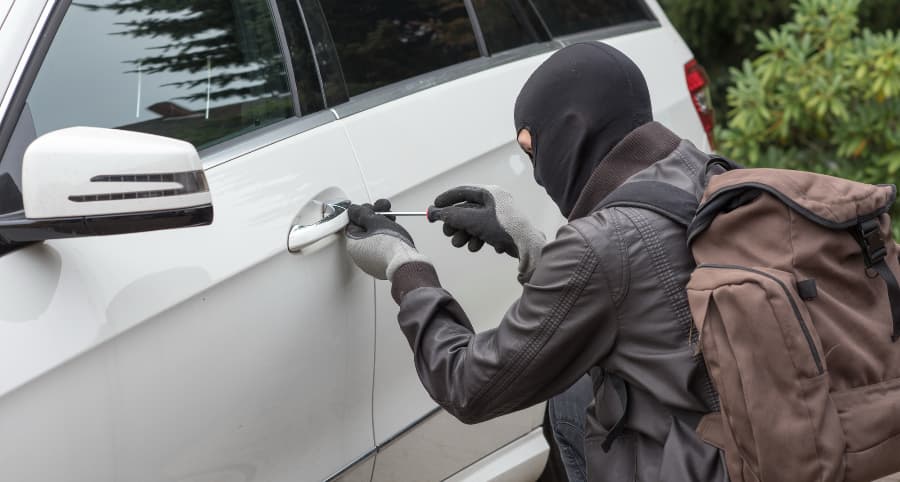 Thief breaking into a white car in a residential area